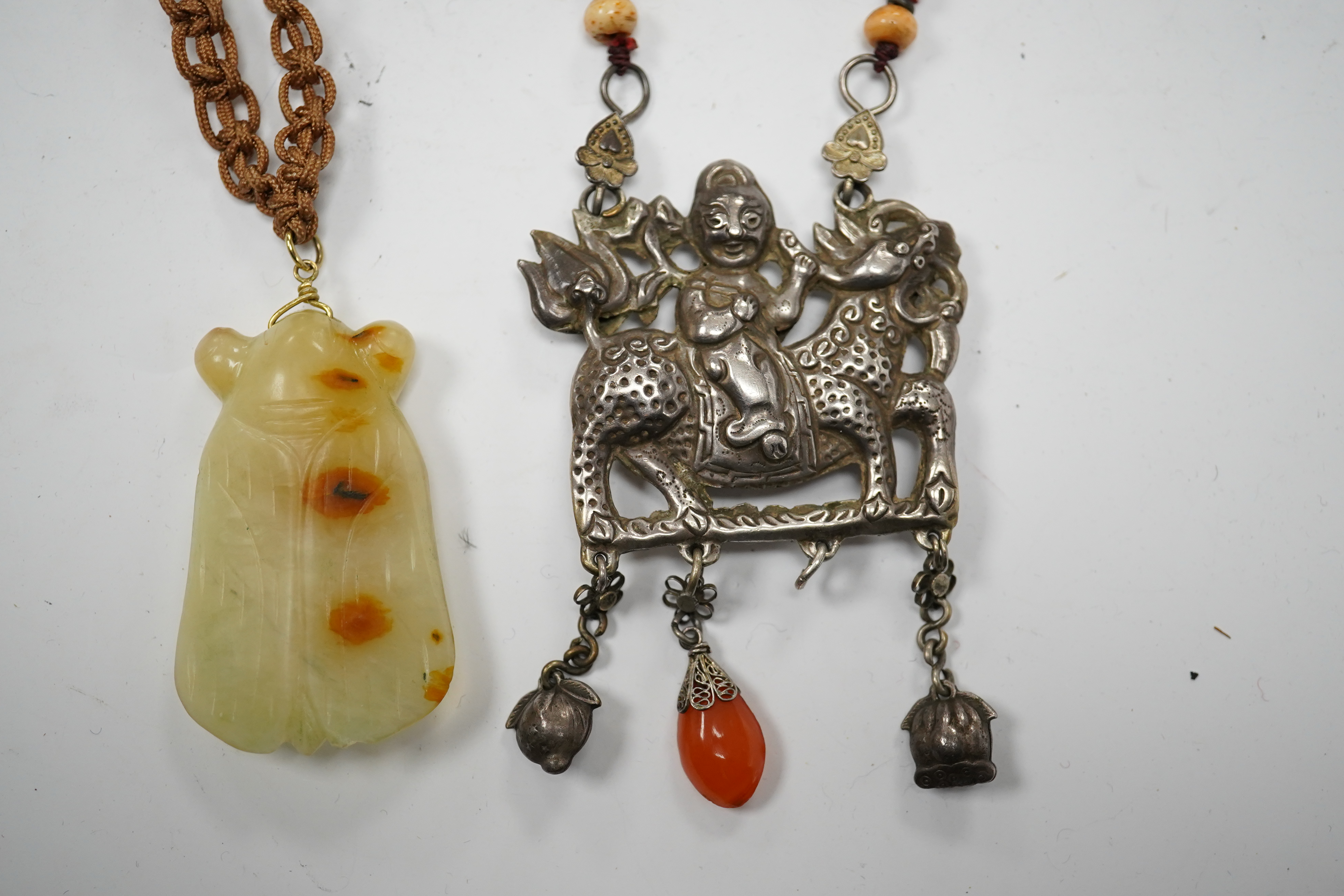 A Chinese celadon and russet jade cicada pendant on cording and a silver and stone mounted chain and pendant of boy riding a qilin, cicada 5.5cm long (2). Condition - tip of cicada wing chipped and on silver pendant one